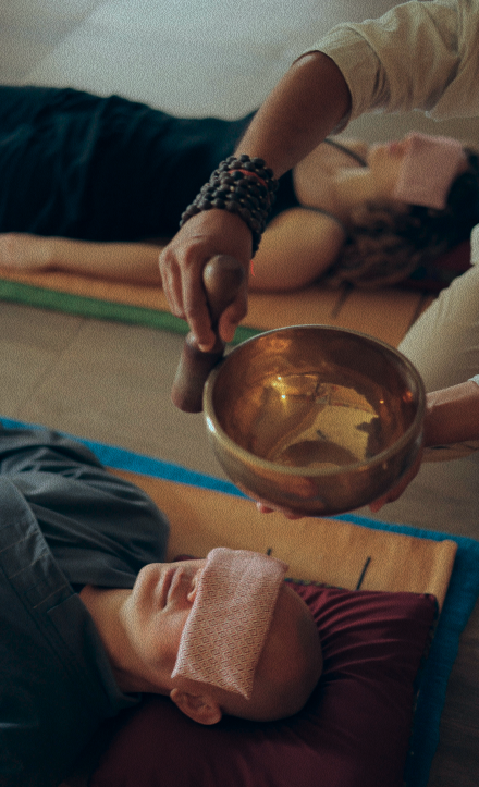 A practitioner holding a singing bowl over a person lying down during a sound healing meditation session.